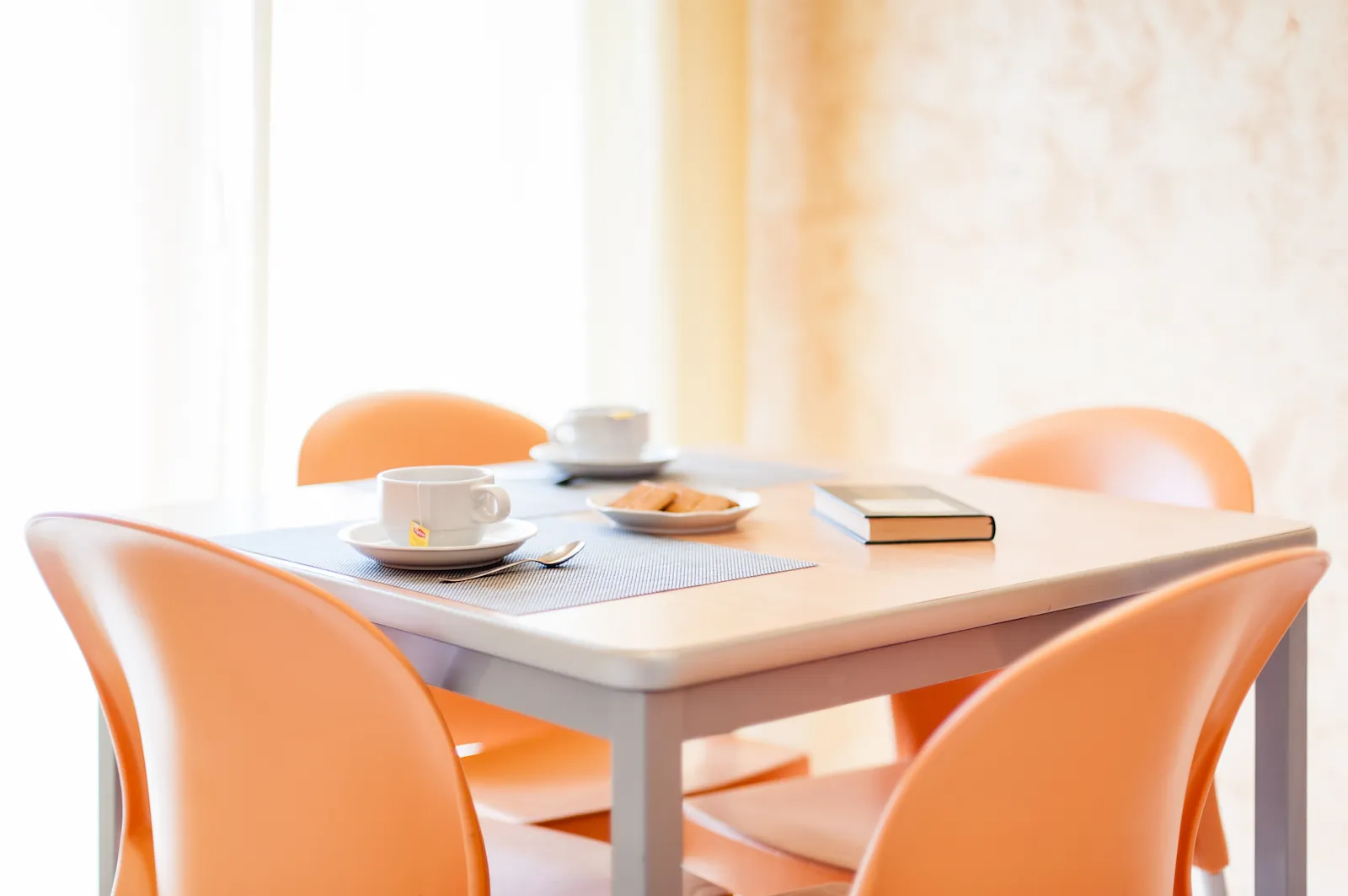Dettaglio di un tavolo apparecchiato per la colazione, sullo sfondo una porta-finestra che conduce al balconcino